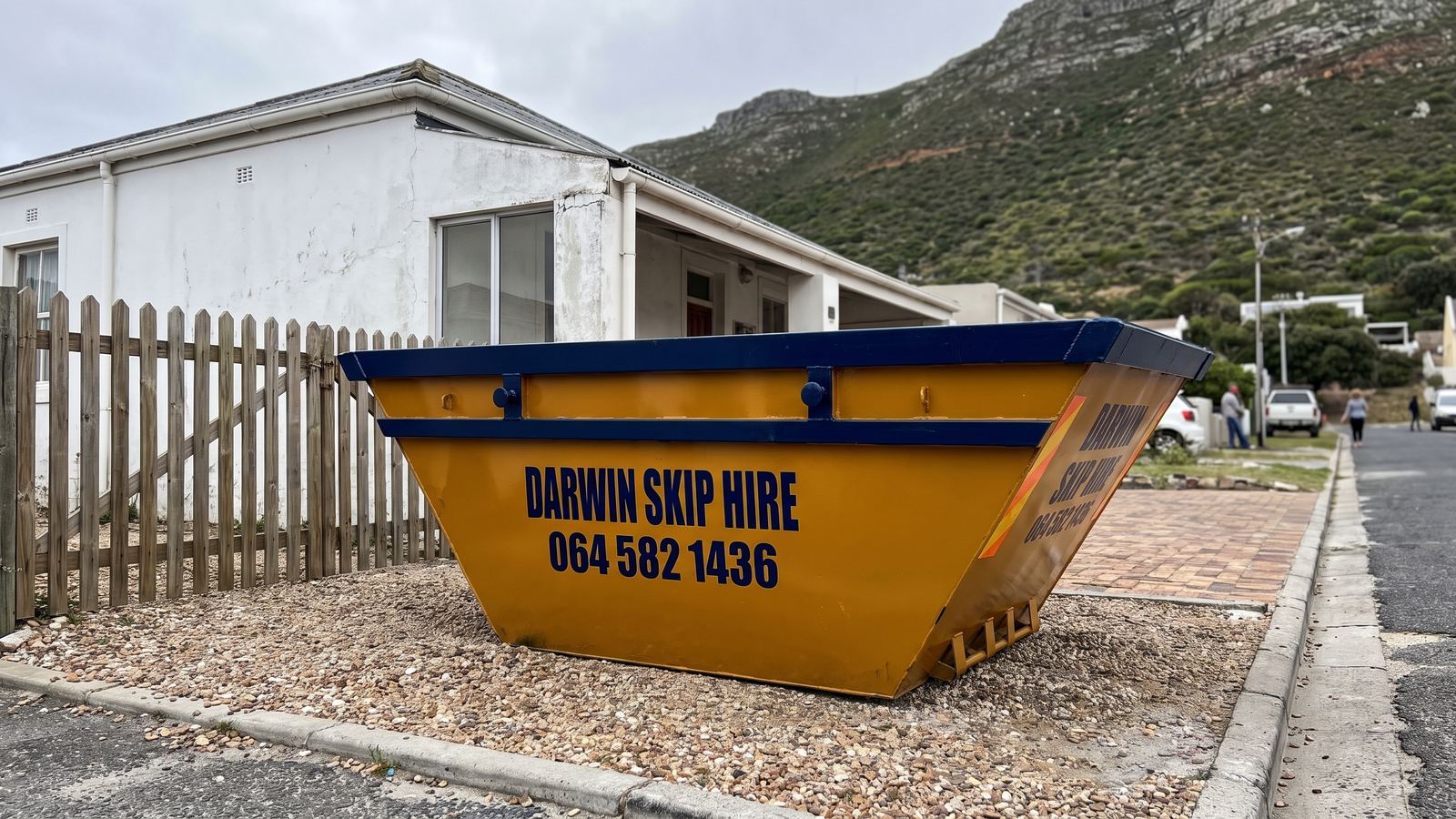 Amber Darwin mini skip on the gravel driveway of a coastal cottage below a fynbos slope.