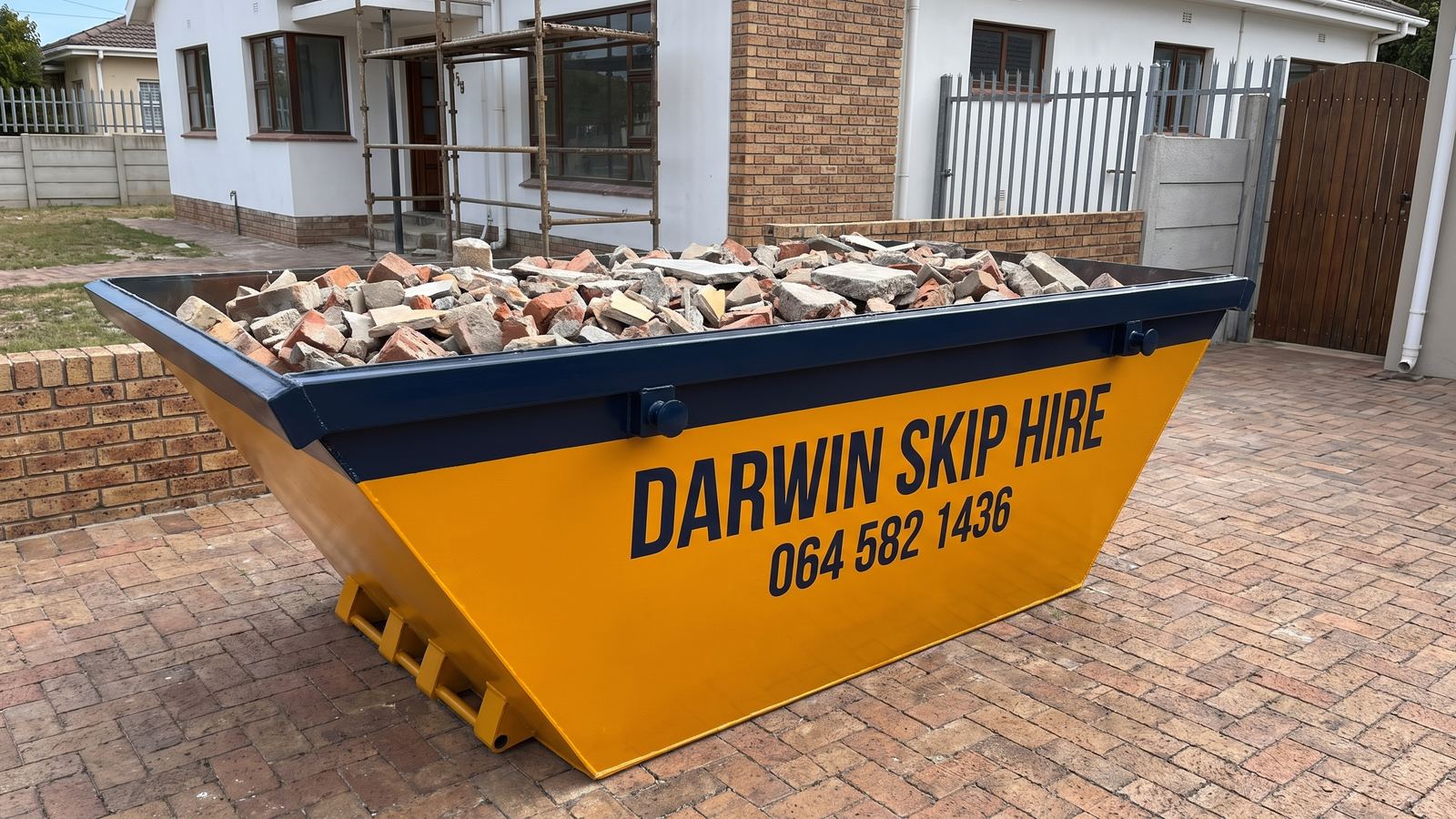 Darwin mini skip filled level with broken bricks on a brick-paved driveway.