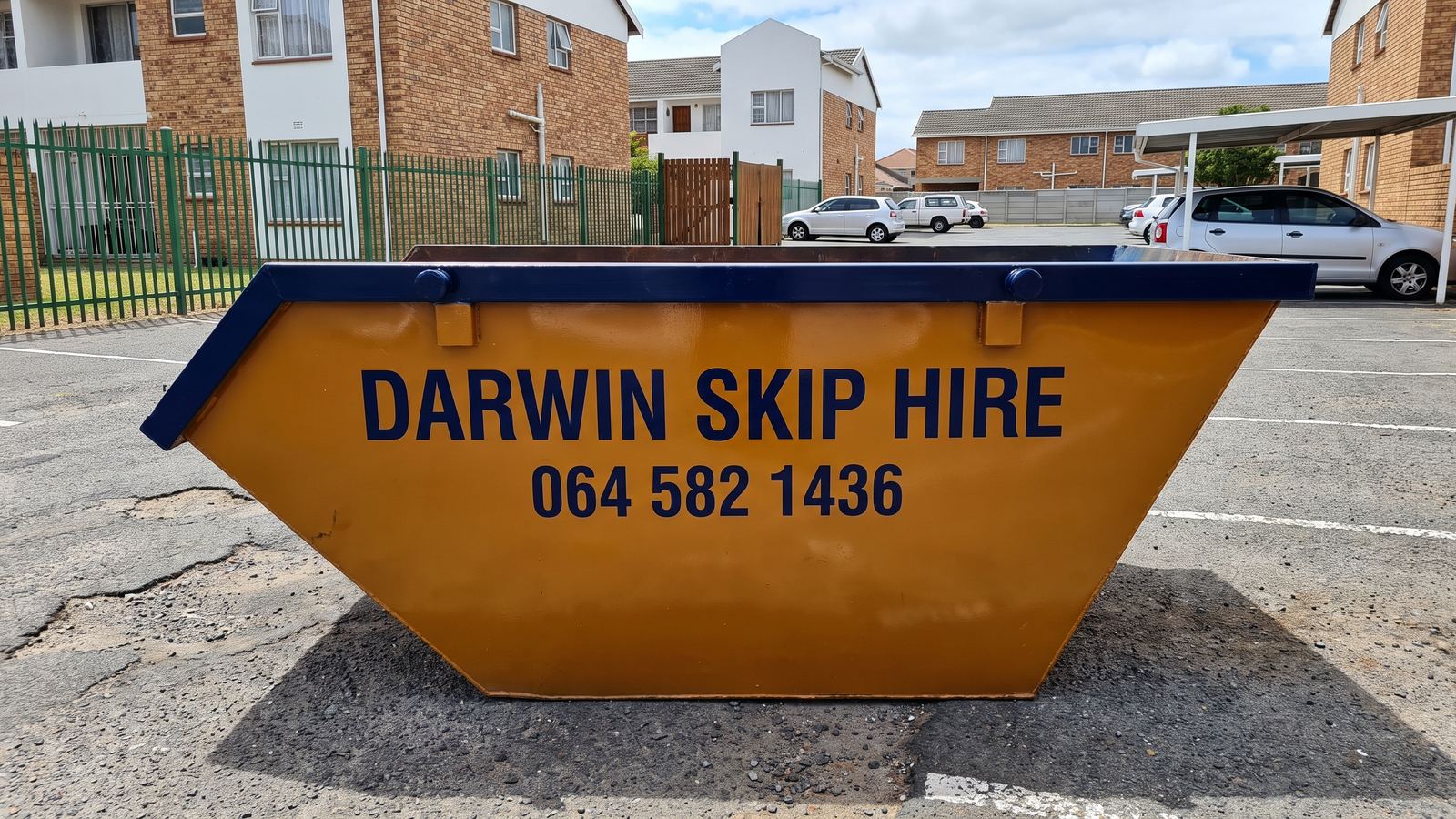 Amber Darwin mini skip in the open parking area of a townhouse complex.