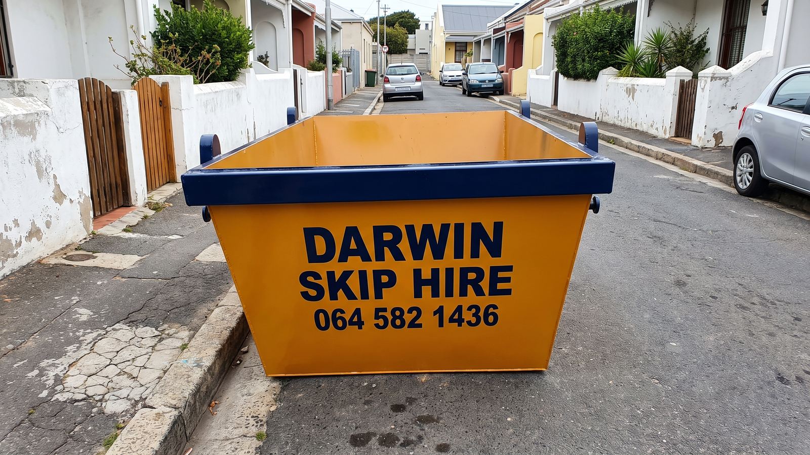 Amber Darwin mini skip against the kerb of a narrow street of terrace houses.